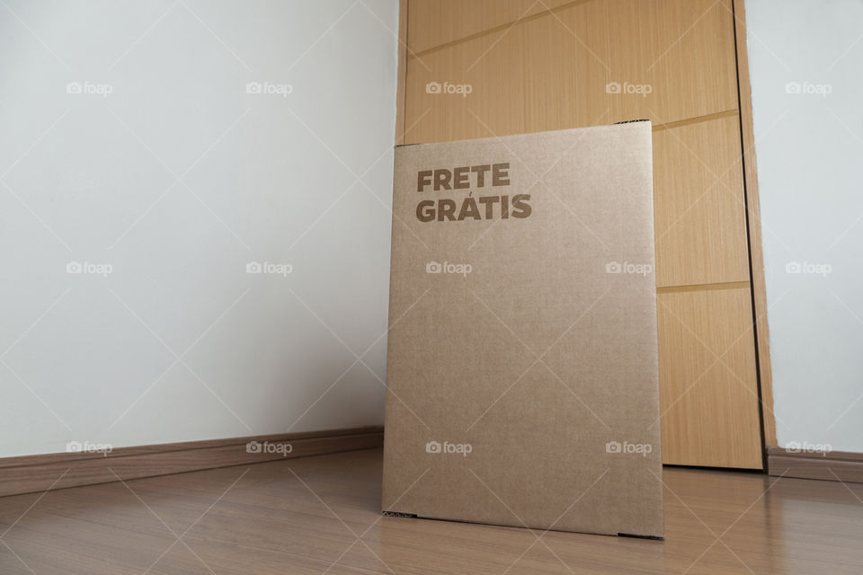 Detail of man with black gloves holding a cardboard box written free shipping to deliver products on gray background. Delivery concept. Delivery service concept. Copy space. Black friday concept.