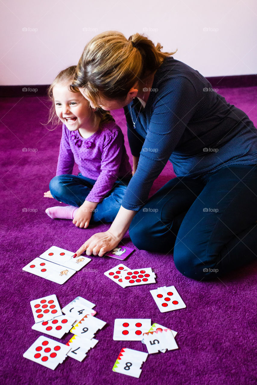 Mother teaching counting her little daughter using card game sitting on a carpet at home