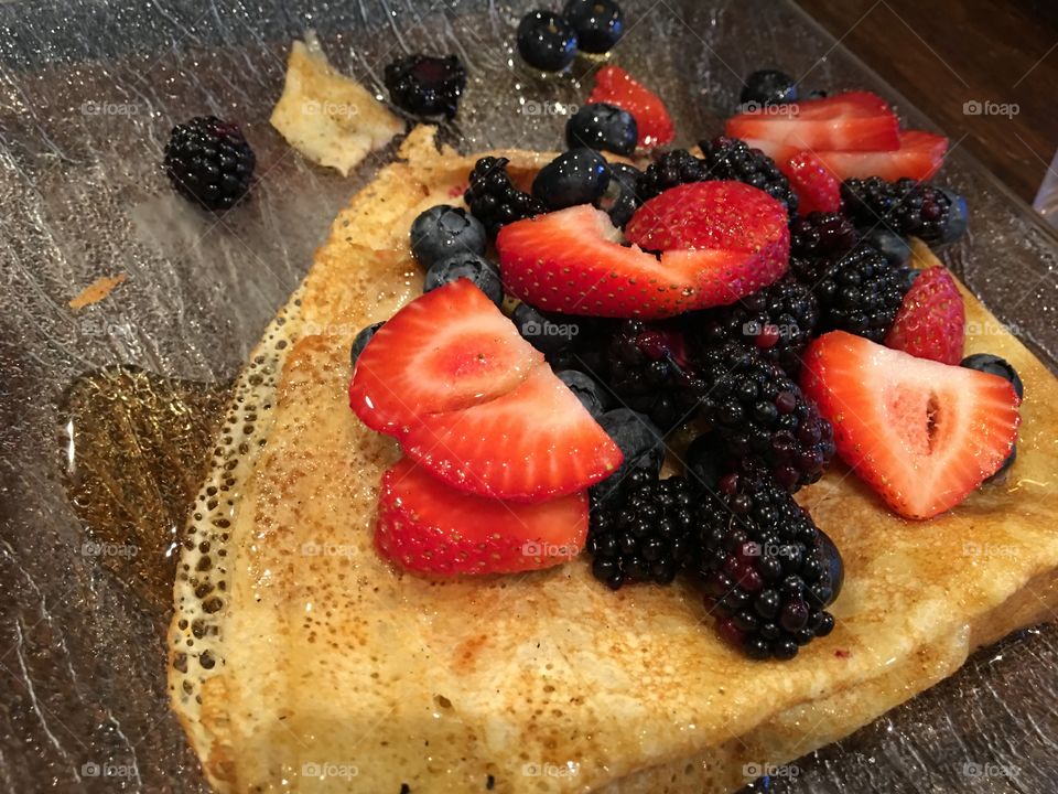 Beautiful fresh  antioxidant rich summer fruit on crepe with maple syrup berry types are Blackberry, Strawberry and blueberry on wood table surface 