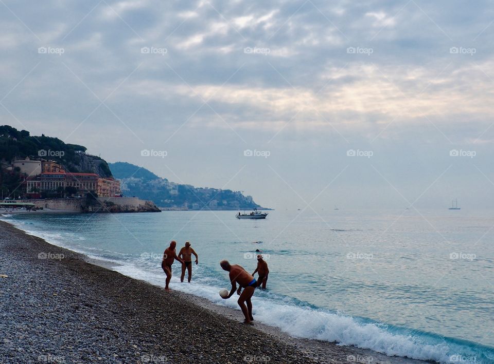 Elderly men playing with a ball on the pebble beach in Nice, France on an early fall morning.