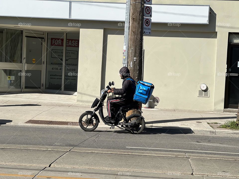 Food delivery driver on a scooter in the city on the road on a sunny September afternoon.