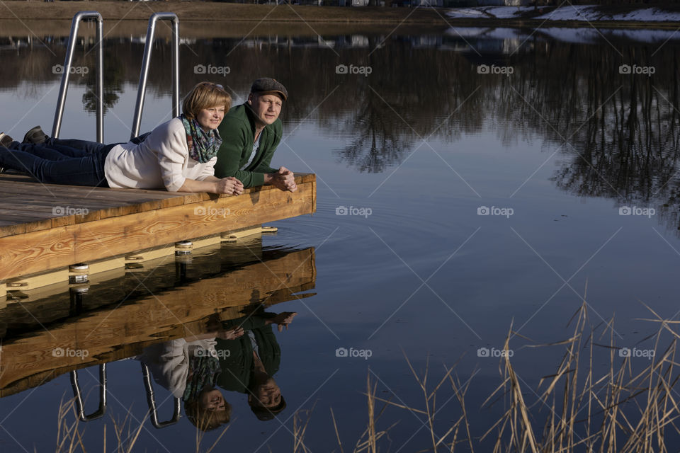A man and a woman lie on the pier on the lake