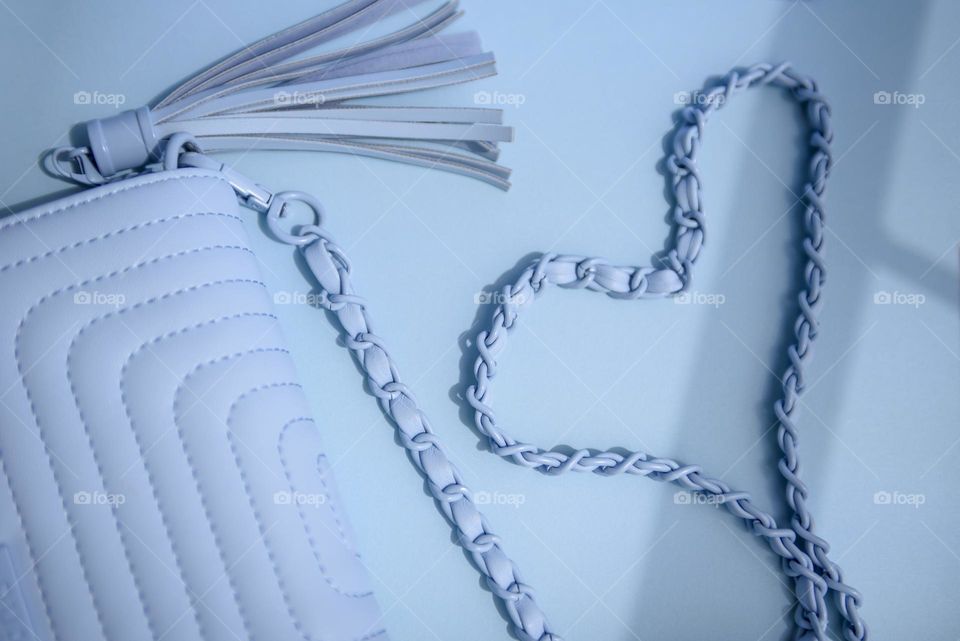 A blue small quilted bag lies on a blue background. The blue chain is laid out in the shape of a heart. View from above