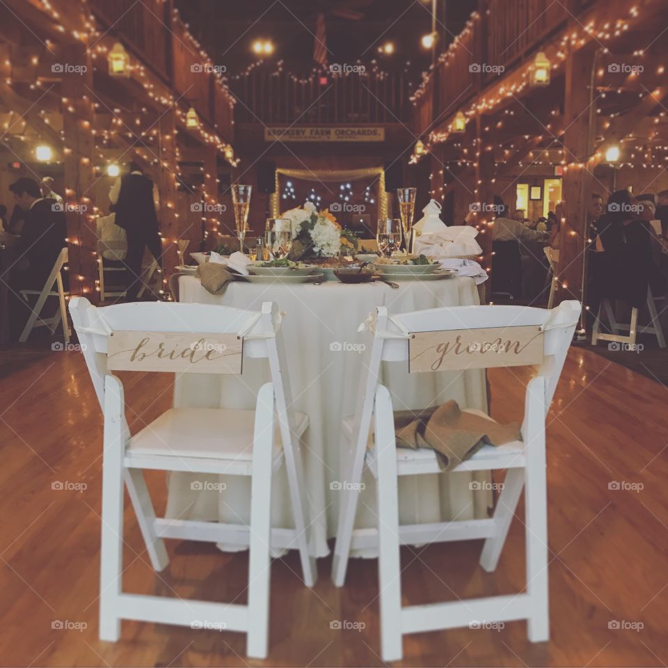 The bride and groom leave their table to go and greet their guests. String lights warm the romantic atmosphere of an old barn. 