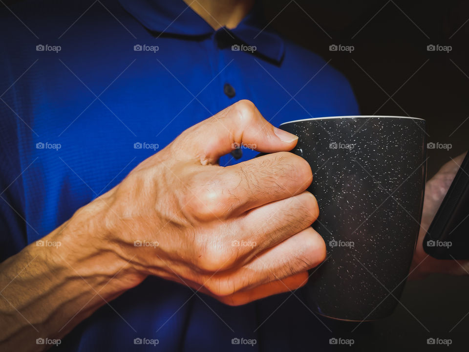 Close up of a man wearing a blue sporty polo shirt and holding his favorite coffee cup; a ceramic fire glazed gun metal gray coffee cup.