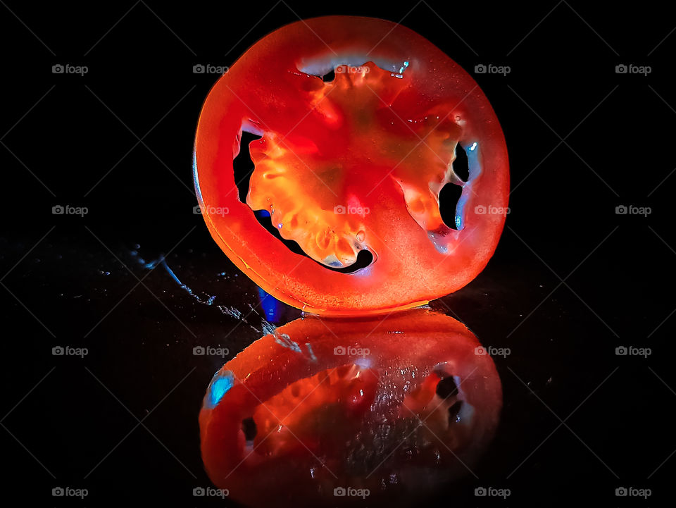 Dark red coloured tomato slice on table top with its reflection having Black background. it is closeup or macro photograph captured in lockdown period.
