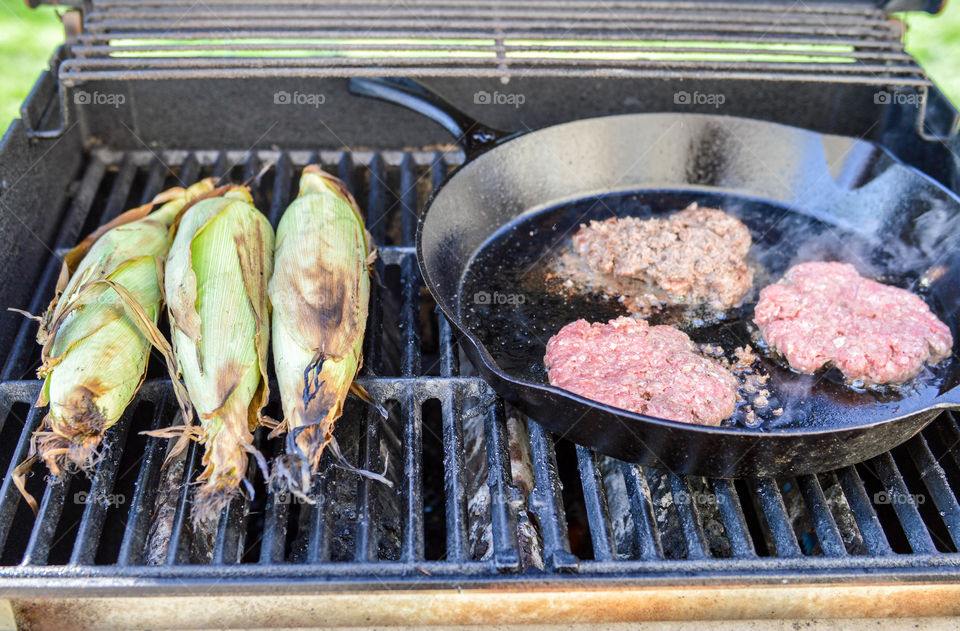 corn on the cob and burgers in a skillet on the grill