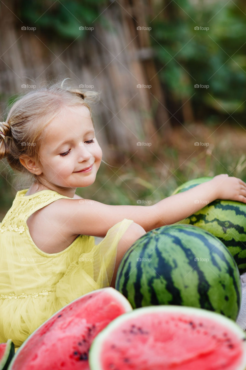 Little girl with blonde hair sitting outdoor with fresh watermelon 