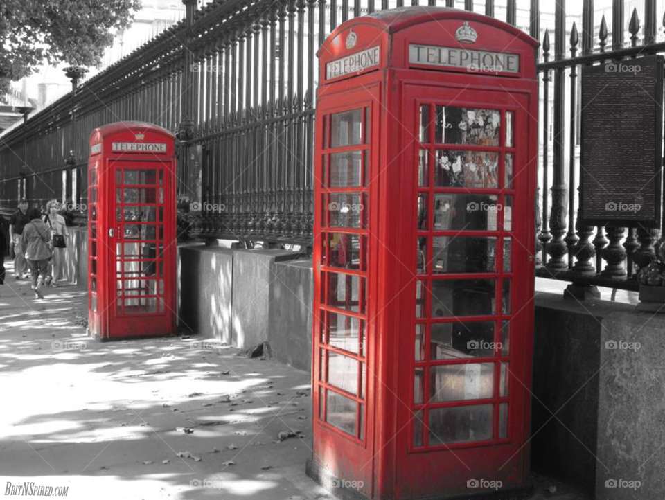 Iconic red London call box / telephone booths, against a black and white background of a garden fence