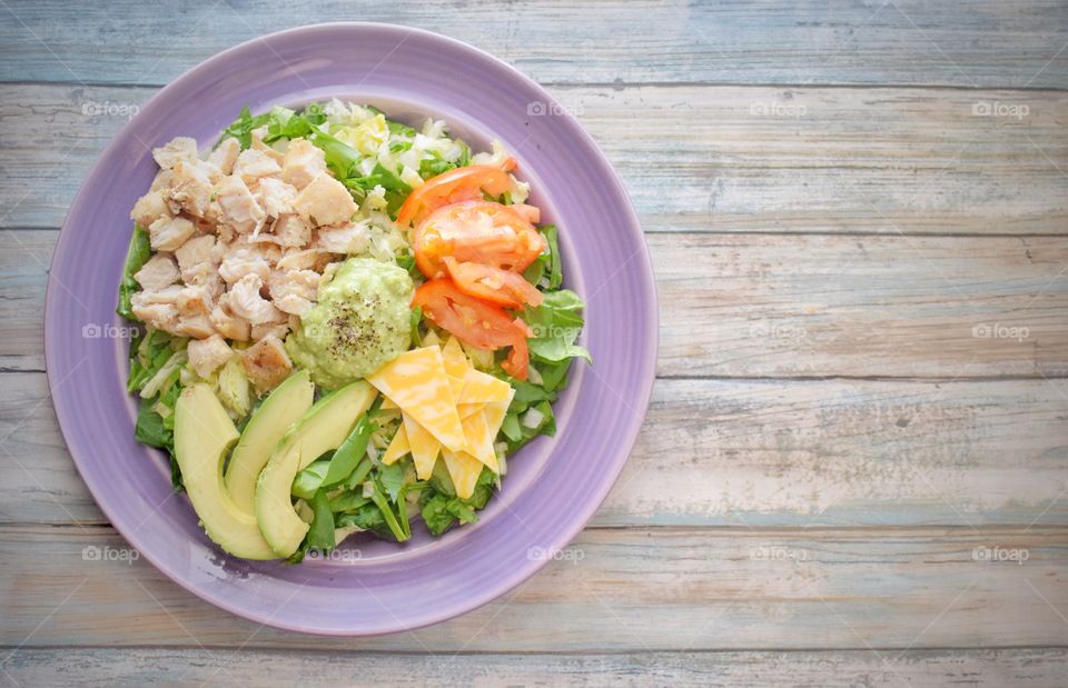 A healthy, colorful plate of salad on a purple plate with wood background social media ready with copy room
