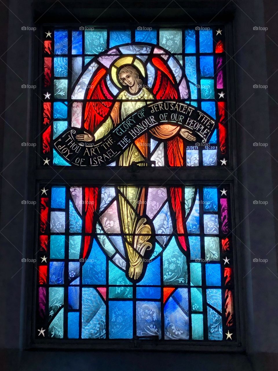 Stained Glass image of angel holding banner honoring Jesus 