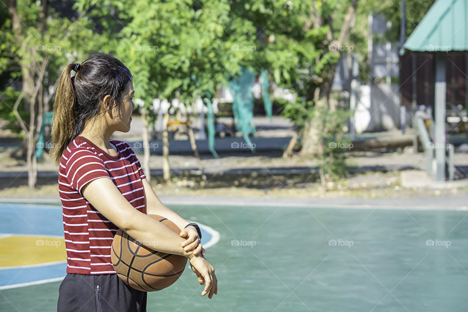 Leather basketball in hand of a woman wearing a watch Background blur tree in park.