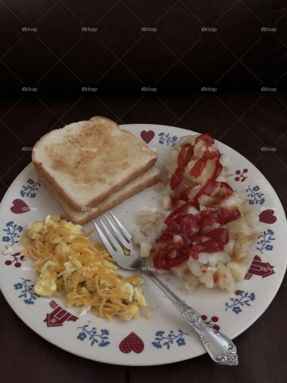 Breakfast: eggs with cheese, hash browns with ketchup and toast with butter 