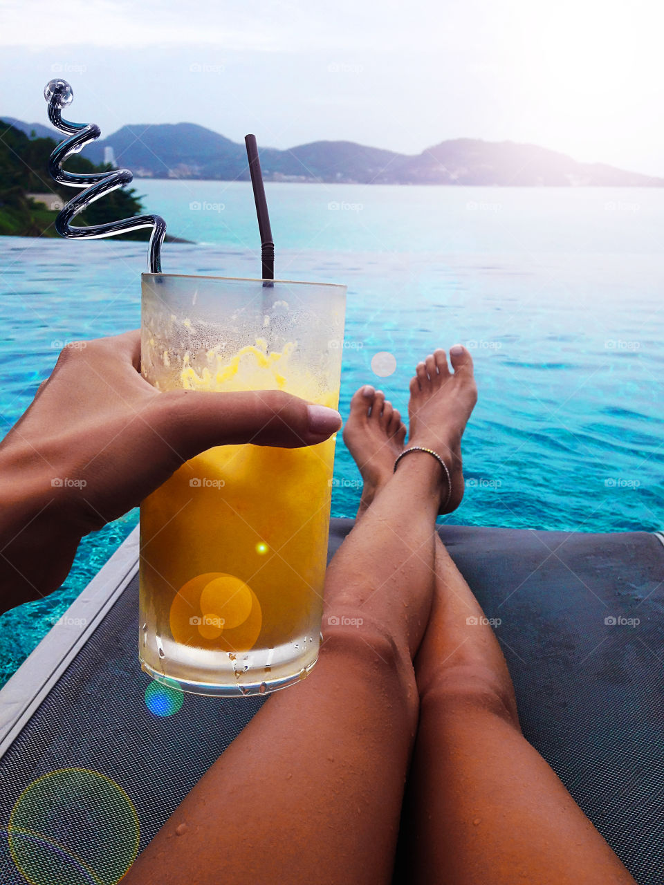 Young woman enjoying a tropical cocktail at the swimming pool above the sea during the summer tropical vacation 