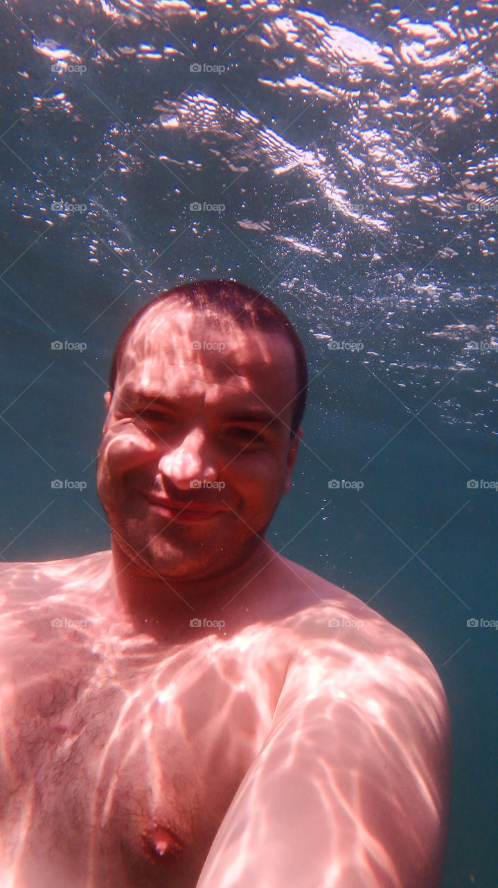 Man diving, man underwater smiling and relaxing in big blue sea