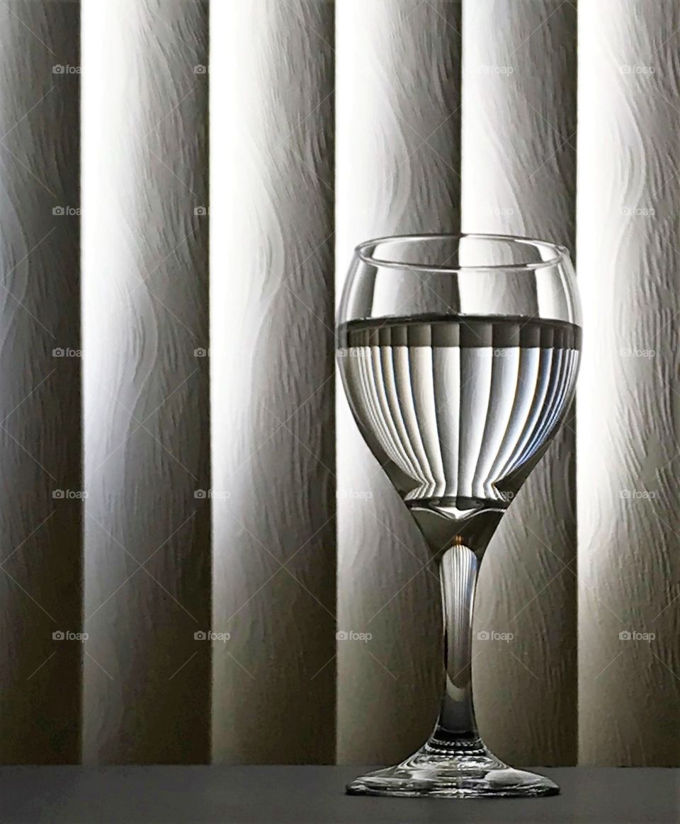 Monochrome, glass sitting in front of window blinds, reflecting pattern into glass