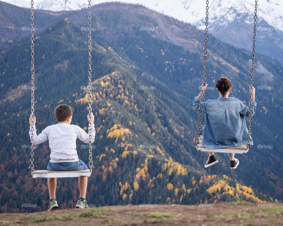 The good moment of older sister and young brother are playing swings to see beautiful mountain scape in autumn season 