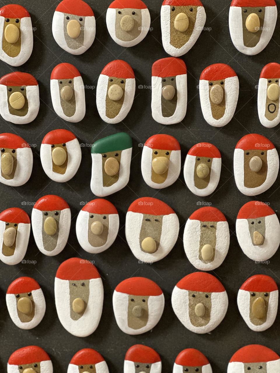 Many handmade stone Santa Claus magnets on a wooden board 