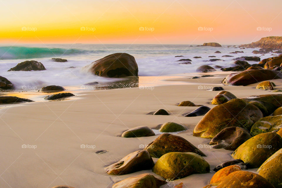 Long exposure of boulder beach with waves at sunset.