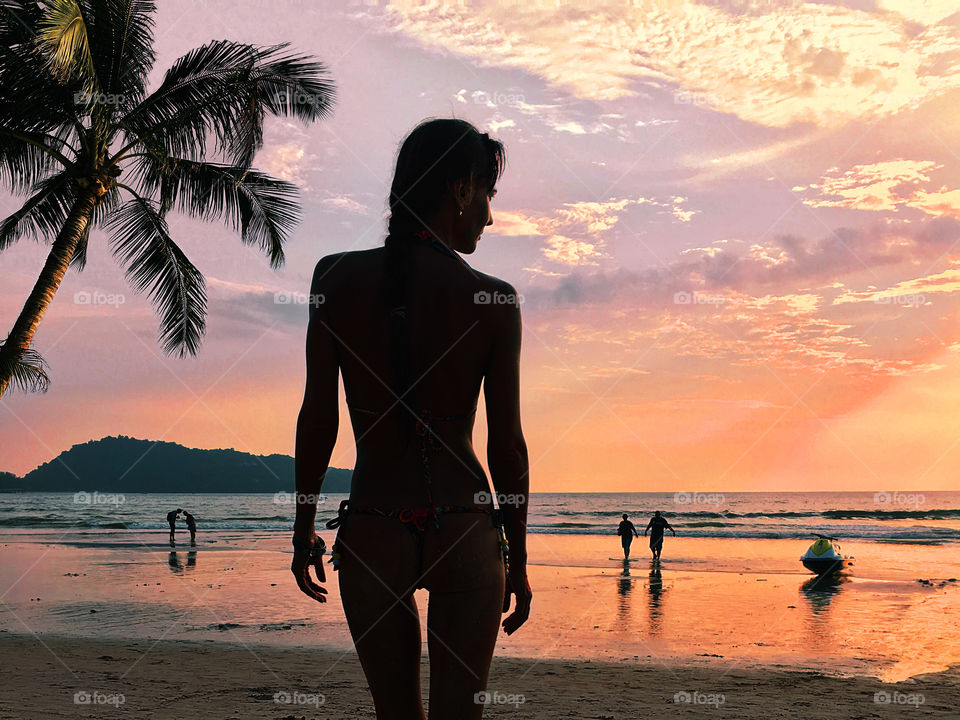 Silhouette of a young woman at the tropical beach with palm trees at sunset time 