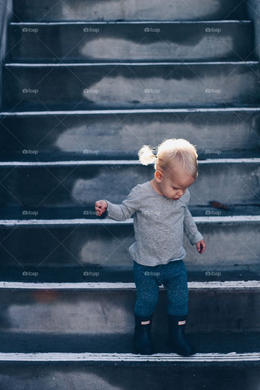Toddler on stairs on a rainy day with the sun shining on her pig tails
