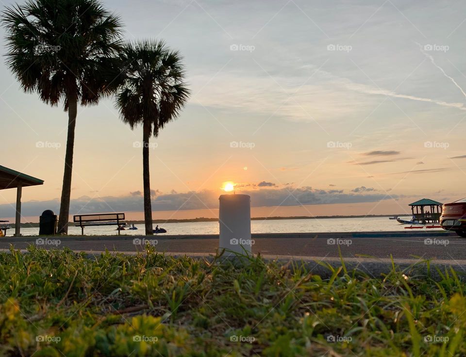 Candle By Palm Trees And The Water Seems To Be Lit Up With A Small Flame From The Sun Setting.