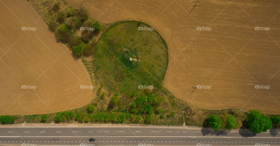 Round piece of grass on a plowed field near the road. 