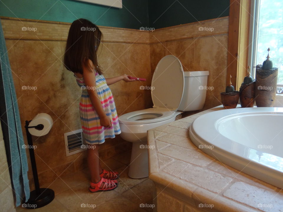 Careful. Little girl playing with cell phone over open toilet in bathroom