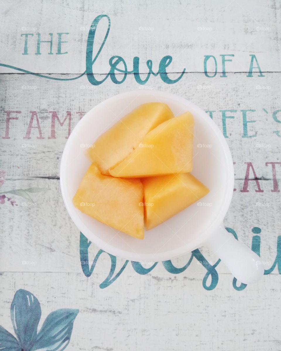 Chunks of Cantaloupe are in a saucer that is on a placemat that reads "The love of a family is life's greatest blessing"