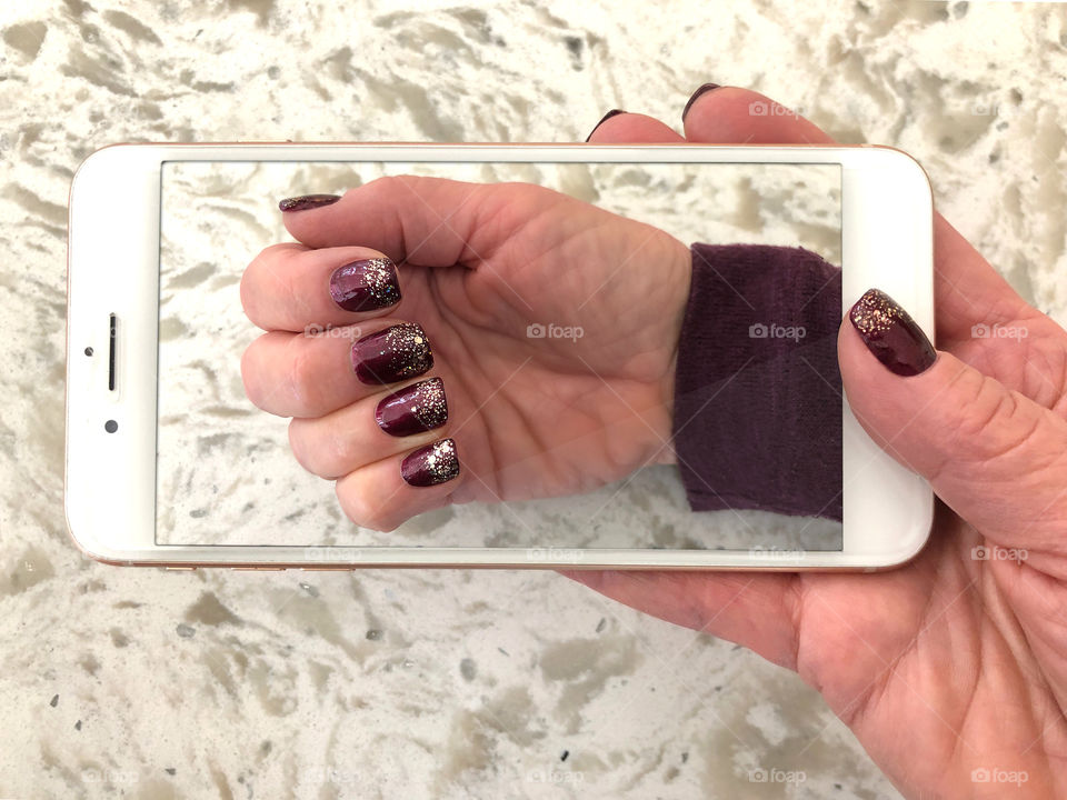 A gel manicured hand holding an iPhone with a photo of the same manicured hand.