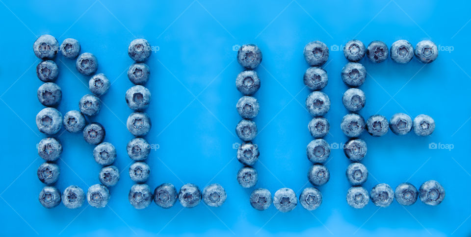 Blueberries on blue background spelling the word blue. Letters, word, fresh, fun, food, nutrition, berry themes