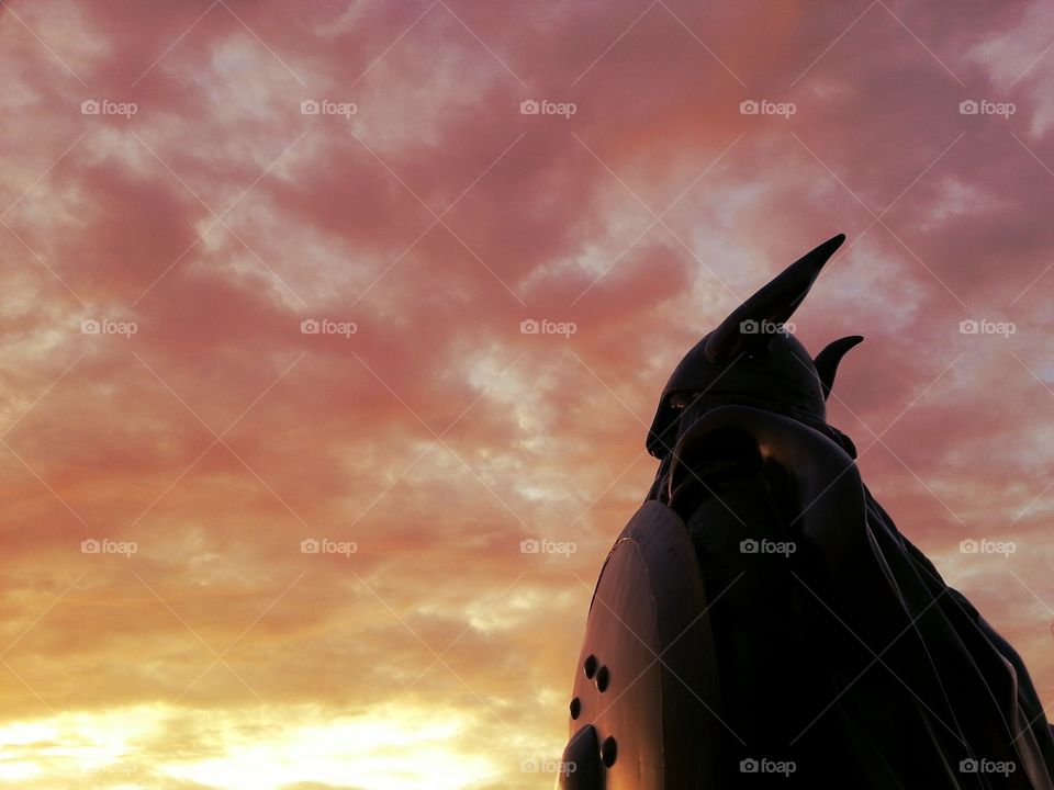 A statue welcomes a glowing sky above.