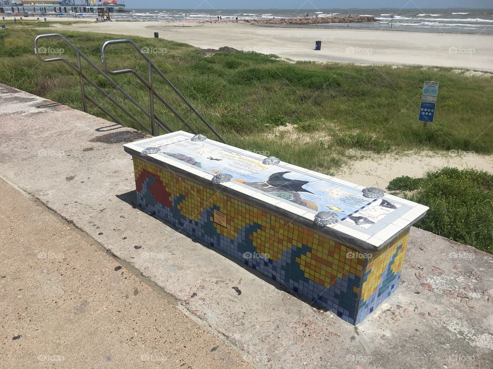 One of many tiled benches alongside the shoreline of the Galveston Island beach. A manta ray can be seen on the surface.