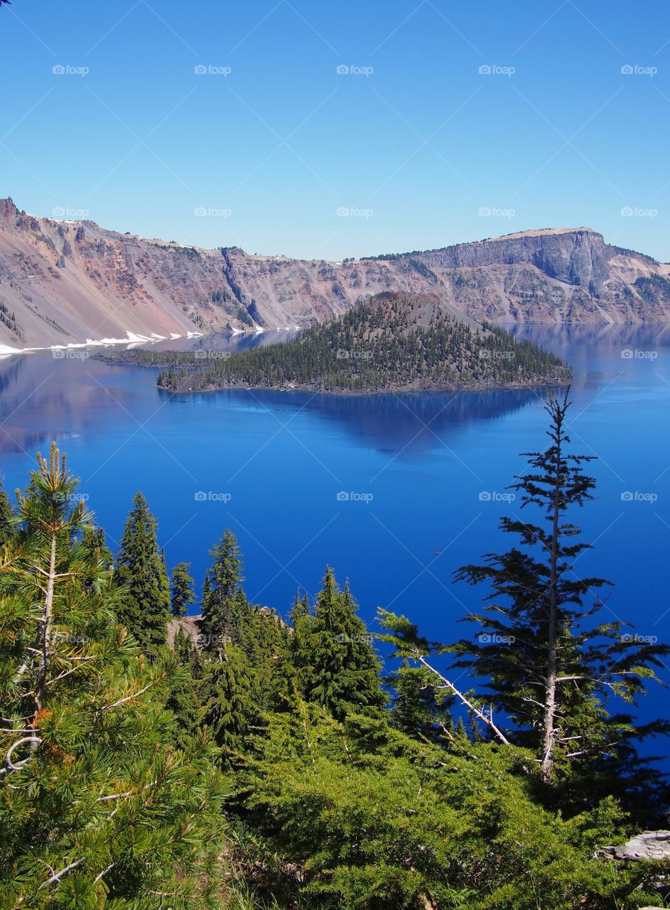 The jagged rim reflecting into the rich blue waters of Crater Lake in Southern Oregon on a beautiful summer morning with perfect clear blue skies. 