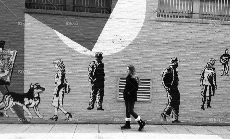Woman walking on street near graffiti wall