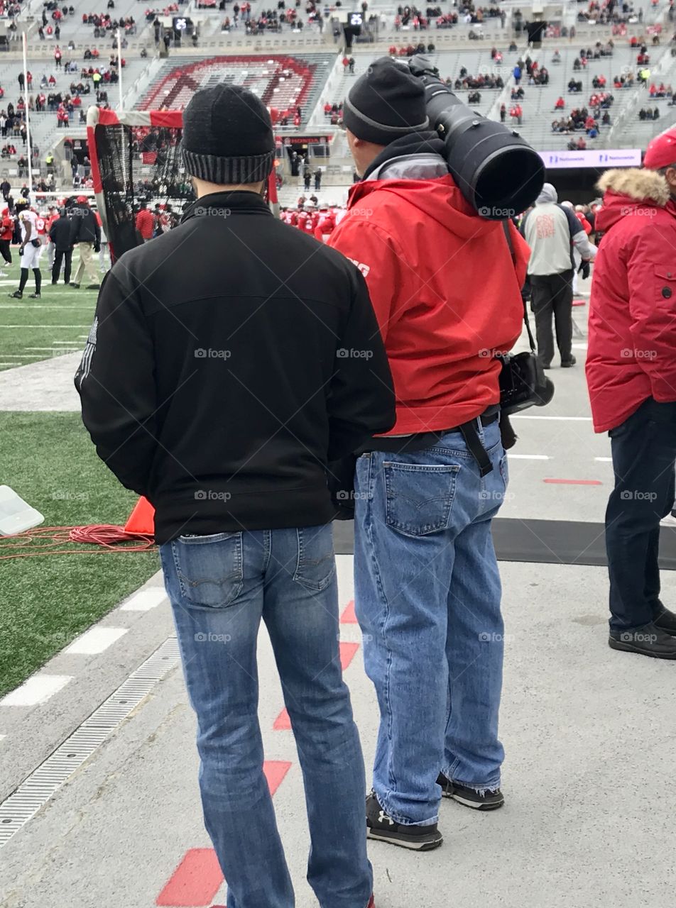 Professional photographer with a huge lens on his camera getting ready to photograph a football game