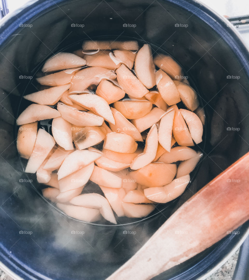 Slices of quince bubbling away in a deep, blue pot and wooden spoon to hand