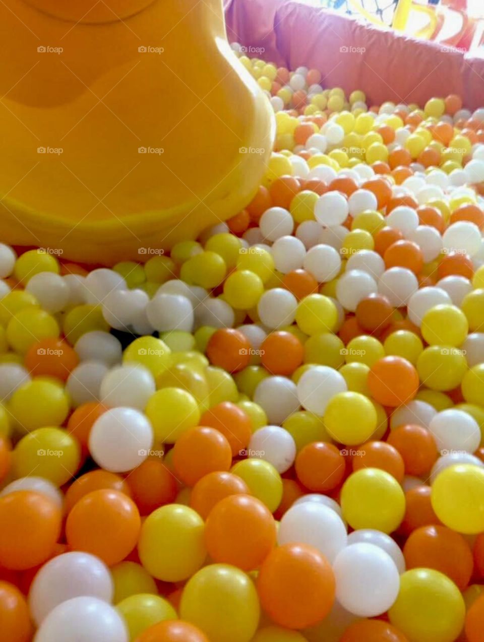 A yellow slide opens up into a ball pit full of orange, white, and yellow balls. 