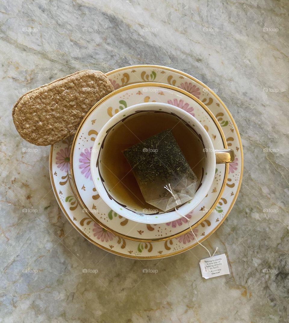 Cup of tea with tea bag and biscuit on counter 