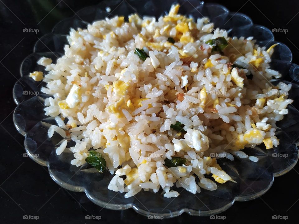 Simple fried rice with egg, garlic and chili mix.  Served on a transparent glass plate with a black background