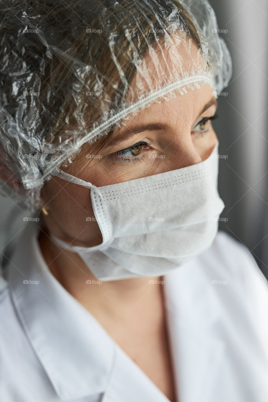 Doctor with face covered with mask. Portrait of young woman wearing the uniform, cap and mask to avoid virus infection and to prevent the spread of disease. Real people, authentic situations