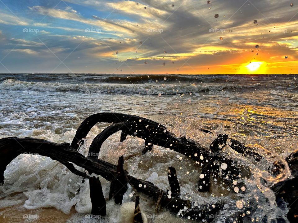 A breathtaking sunset as the waves, often towering and frothy, collide with the shore with great force, sending spray and foam into the air creating a stunning display of energy and motion