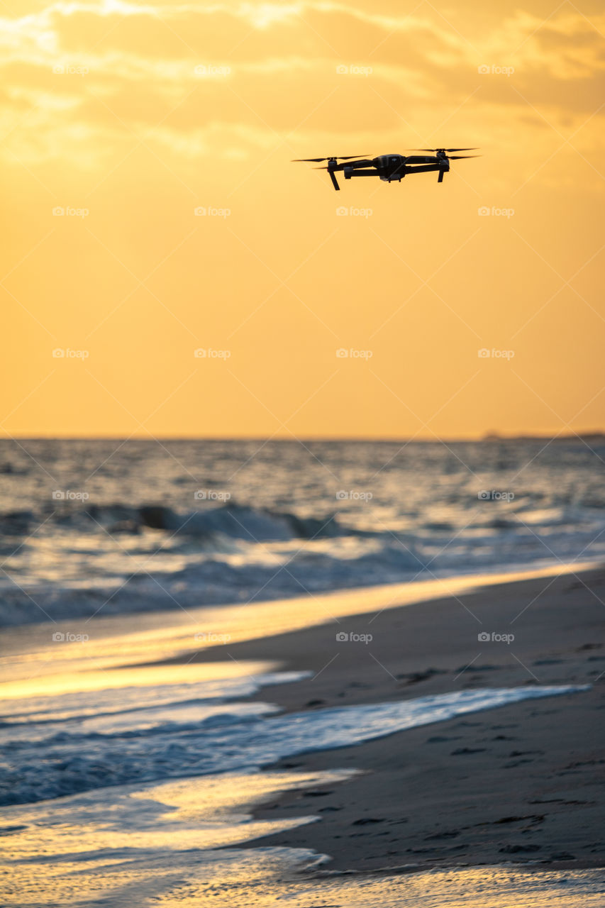 A drone capable of taking 4K video and RAW format photos, flying over a pristine beach as the sunset illuminated the scene in golden light.