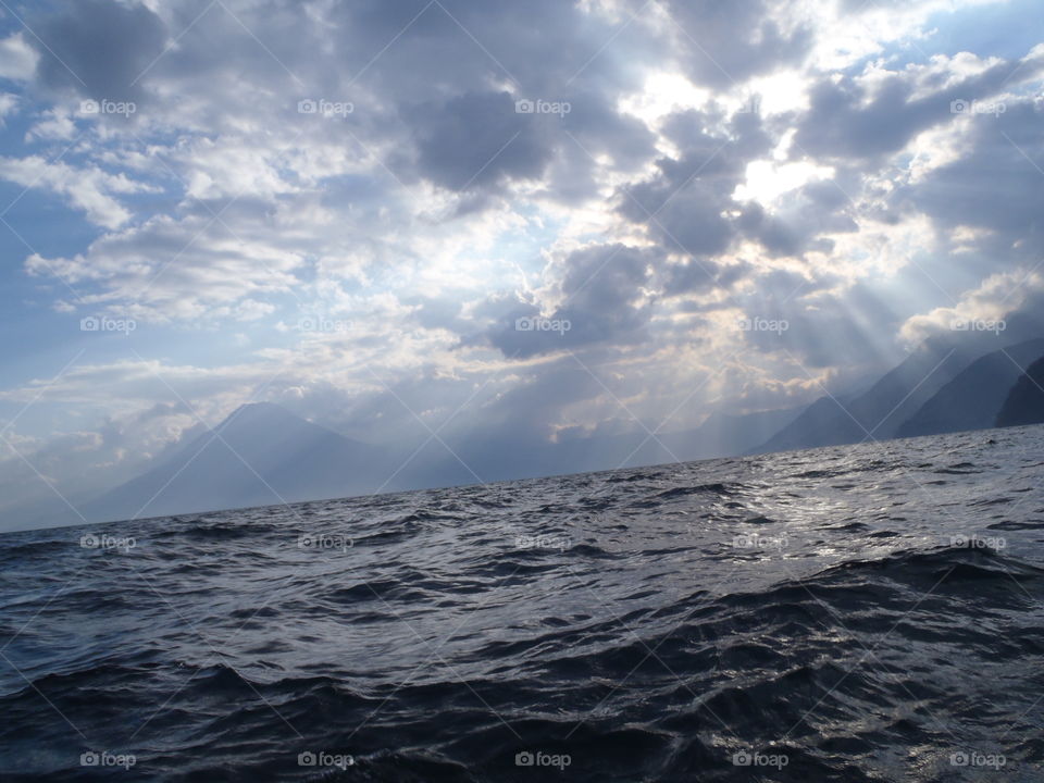 Sun rays over lake. Lake Atitlan waves below sun shining through clouds