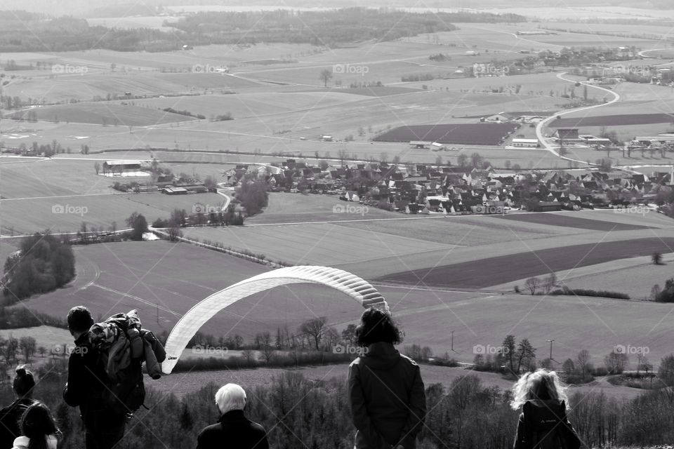 Black and white photo of a group of people watching a paraglider glide over a landscape