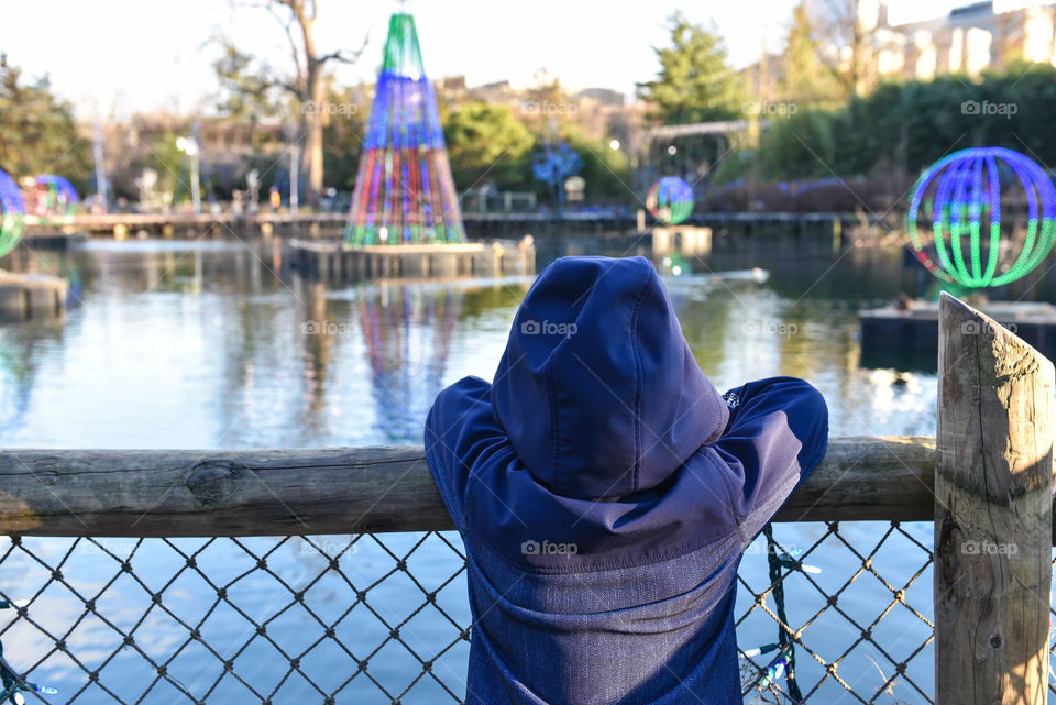 Young child leaning on a railing to look at Christmas holiday lights on a lake