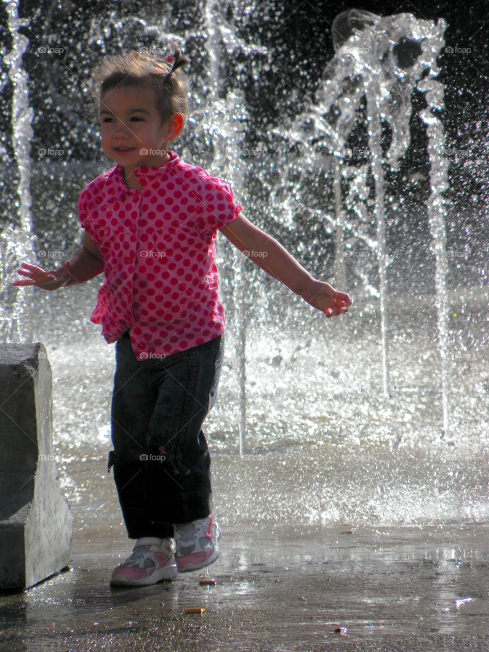 Little girl being playful with the splashes of the water fountain
