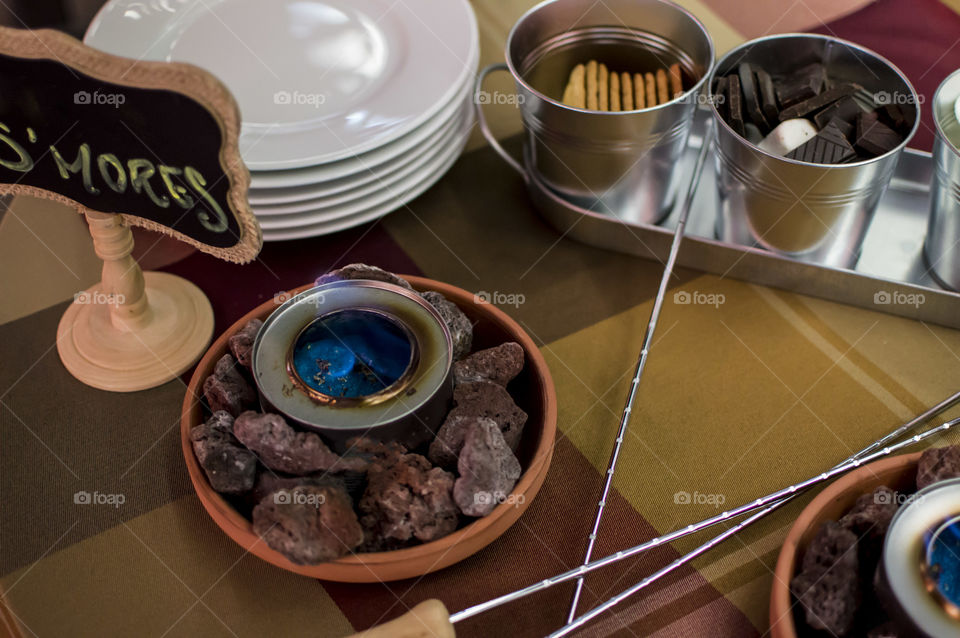 S'mores bar at summer party with skewers, dark chocolate, flame, burners, sign with the word s'mores in handwriting on chalkboard fun summertime party or campfire conceptual background