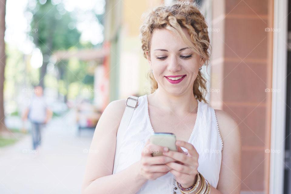 girl smiling and typing on the phone. curly blnd girl smiling while typing on her phone
