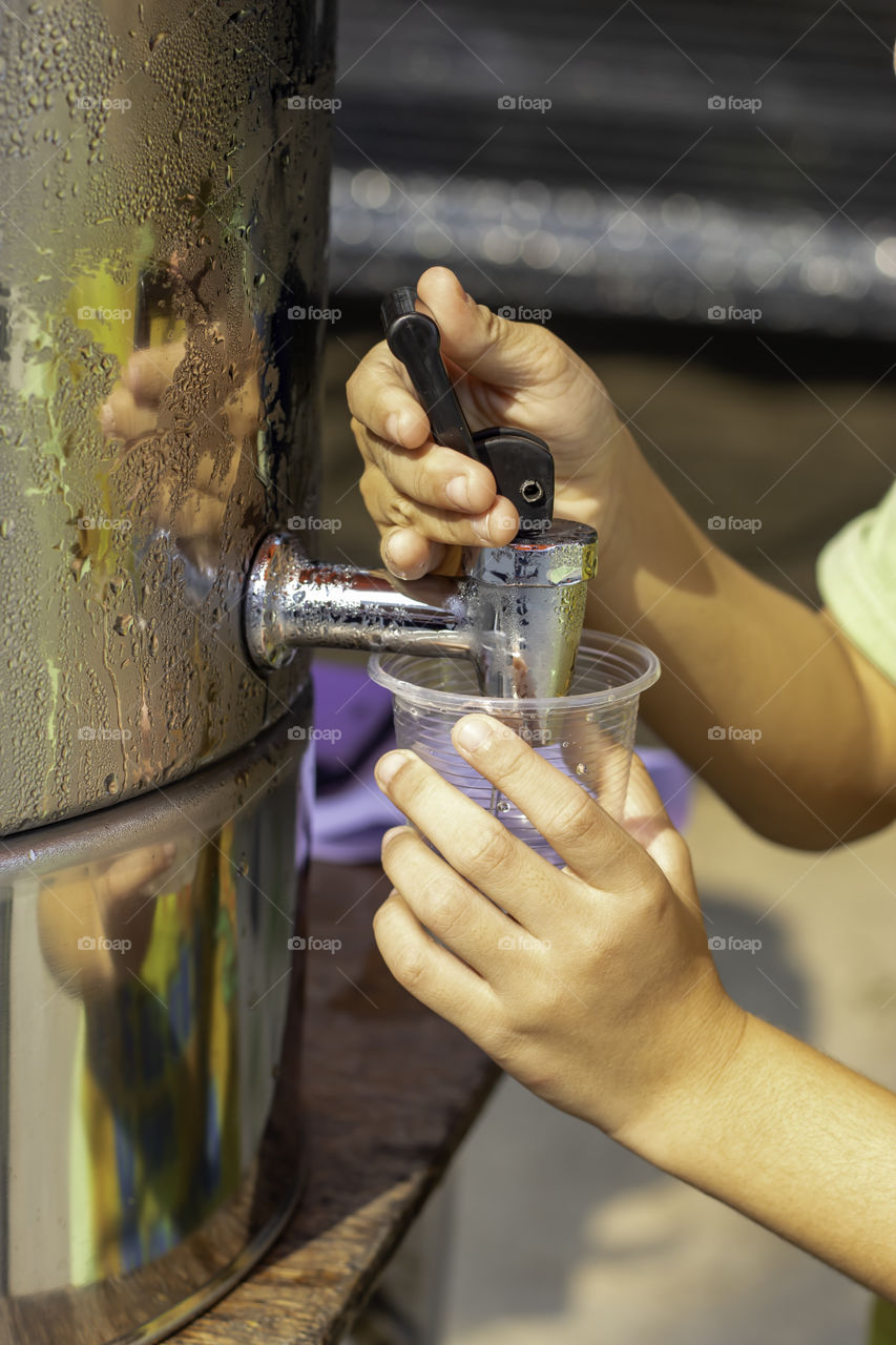 Hand boy holding the glass with water from the water cooler.